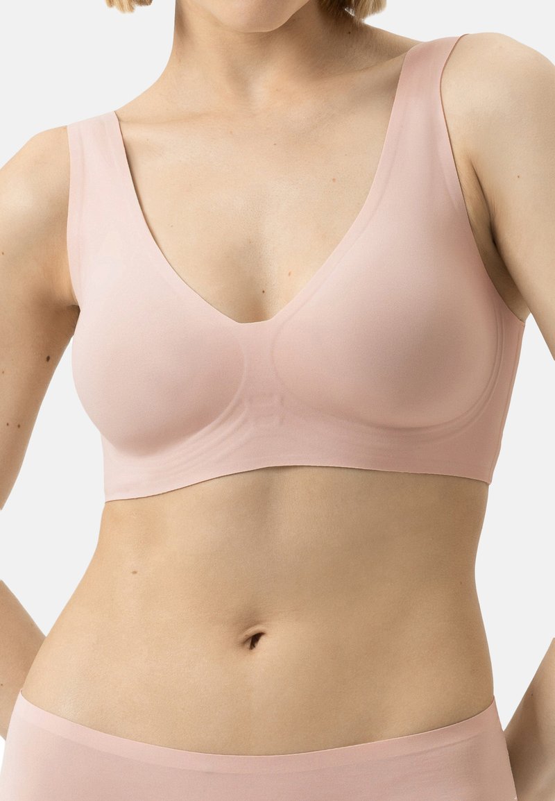 Zacht roze stof bralette met een diepe V-hals, brede bandjes, naadloos ontwerp en subtiele textuur. Lichtgewicht en vormgevende pasvorm.