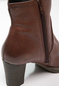 Bottine en cuir marron avec talon bloc empilé et détail de fermeture éclair latérale sur fond blanc.