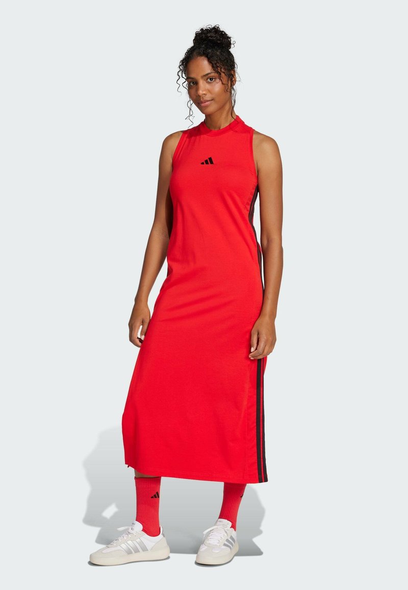 Red sleeveless dress with side black stripes, made from a smooth fabric. Paired with white sneakers and red socks, featuring black accents.