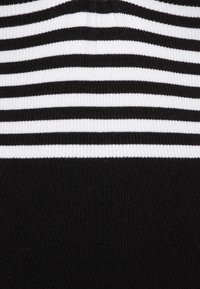 Haut en tricot présentant des rayures horizontales noires et blanches, avec une texture côtelée et une section inférieure unie noire, offrant une séparation nette dans le design.