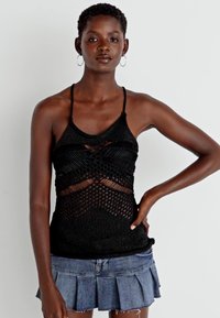 Μαύρη πλεκτή αμάνικη μπλούζα με περίπλοκα πλέγματα, με λεπτές τιράντες και εφαρμοστή σχεδίαση, συνδυασμένη με τζιν φούστα.