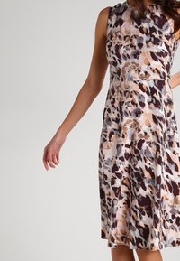 Mönstrad ärmlös klänning med åtsittande byst och utsvängd kjol. Har ett abstrakt mönster i nyanser av brunt, beige och grått.