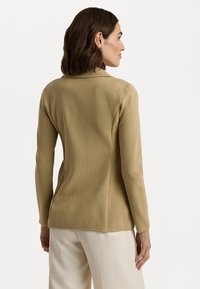 Beige, langermet topp laget av teksturert stoff med en skreddersydd passform. Har krage og lett utsvingt kant. Synlige sømdetaljer.