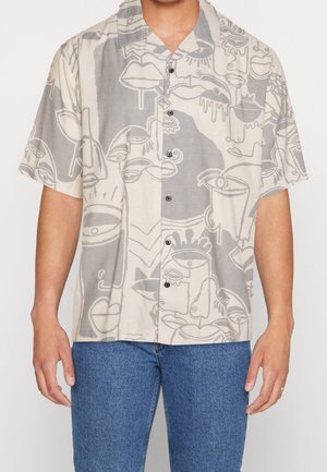 Camicetta a maniche corte in tessuto beige con illustrazioni astratte grigie di volti, tazze e labbra. Cinque bottoni neri sul davanti.
