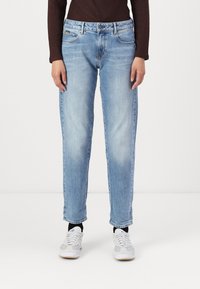 Vaqueros de mezclilla azul claro con un corte recto, diseño de cinco bolsillos y una textura ligeramente desgastada, combinados con zapatillas blancas y grises.