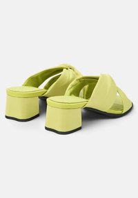 Mule con tacco verde lime con tomaia in tessuto morbido, caratterizzate da cinturini intrecciati e un tacco grosso e stratificato con base nera.