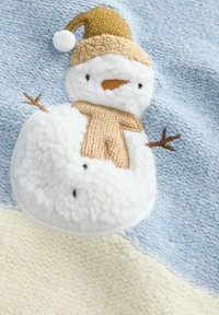 La couverture en peluche présente un design de bonhomme de neige avec un chapeau en tricot beige, un corps moelleux blanc et un fond bleu texturé avec des motifs subtils.