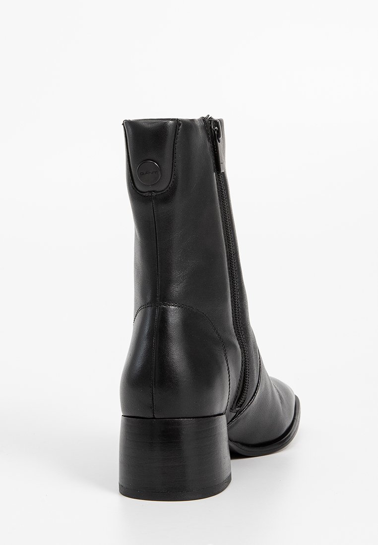 Stivale in pelle nera alla caviglia con punta tondeggiante, chiusura con zip laterale e tacco basso impilato. Presenta una texture liscia e un design minimalista.