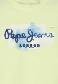 Limetkově zelené tričko s modrou logem ve stylu akvarelu, které zobrazuje nápis "Pepe Jeans" nad "LONDON", s měkkou a hladkou texturou.