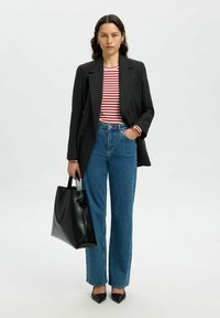 Svart dubbelknäppt blazer över en röd och vit randig skjorta, kombinerat med hög midja jeans i blått, svart tote-väska och spetsiga klackar.