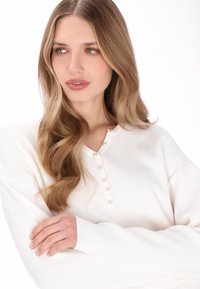 Maglione bianco a coste con scollo henley con bottoni di perla, maniche lunghe e vestibilità rilassata.