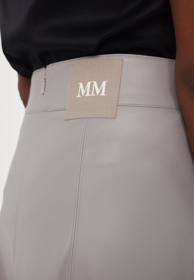 Grå skinnbukser med en glatt tekstur, med en firkantet stoffetikett bak som er preget med "MM" i hvitt. Forsterket sømdetaljer er synlige.