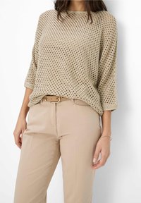Beige, lättviktsstickad tröja med en lös passform, med ett nätmönster och trekvartsärmar. I kombination med beige byxor och ett bälte.