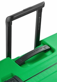 Maleta rígida verde con un acabado texturizado, un asa extensible negra y una correa de transporte negra etiquetada como "UNITED COLORS OF BENETTON."
