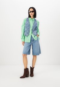 Green and white striped button-up shirt, denim vest, blue denim shorts, and brown heeled boots. Accessories include black sunglasses.