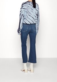 Blue tie-dye long sleeve shirt, navy stripes. Dark blue flared jeans with two back pockets. White ankle boots with block heels.