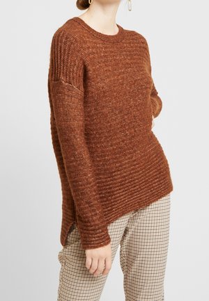 Maglione marrone a maglia con texture a coste, scollo rotondo, spacchi laterali e una vestibilità morbida, indossato sopra pantaloni a scacchi.