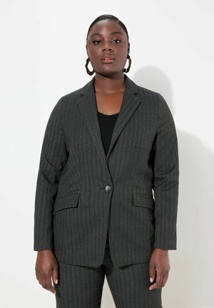 Šedý blazer s proužkem, jedním knoflíkem, dvěma předními kapsami a přiléhavým střihem. Nosený přes černý top, doplněný o odpovídající kalhoty.