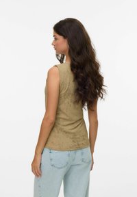 Top senza maniche di colore verde oliva con superficie texturizzata, dotato di scollo rotondo e silhouette aderente, abbinato a jeans azzurri chiari.
