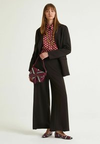 Abito nero su misura con pantaloni larghi, camicia bordeaux a fantasia, borsa viola a fantasia e ballerine coordinate. Gli accessori includono una collana.