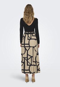 Top negro de manga larga con escote en V, combinado con una falda maxi beige que presenta un atrevido patrón geométrico negro; incluye una cinturilla ajustada.
