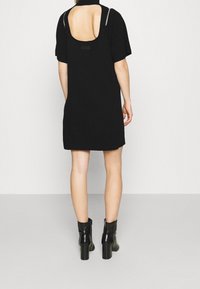 Robe noire à manches courtes, dos ouvert et légère nervure à l'ourlet. Portée avec des bottines noires à talon carré.