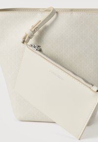 Τσάντα tote Calvin Klein σε ανοιχτό μπεζ με γεωμετρικό σχέδιο. Διαθέτει αποσπώμενη θήκη με λεία υφή, φερμουάρ και λεπτομέρεια με το λογότυπο.