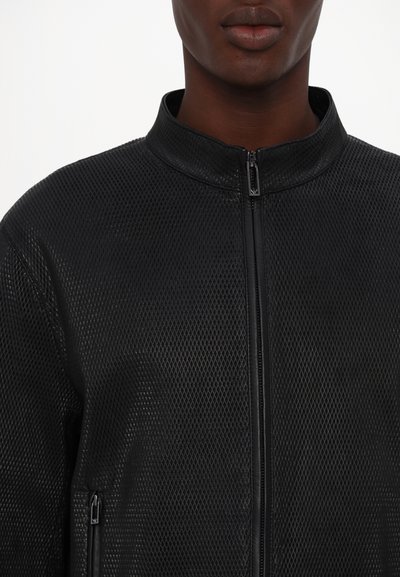 Schwarze Mesh-Bomberjacke mit Reißverschluss, Stehkragen und strukturierter Oberfläche mit Rautenmuster. Mit Seitentaschen.