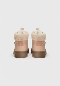 Une paire de bottes d'hiver beiges avec doublure en laine et languettes, présentées de dos sur un fond blanc.