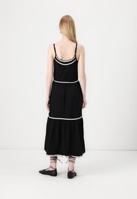 Sort maxi-kjole med spaghetti-stropper, der har hvid tekstureret kant langs buste og kant. Svungent silhuet og lagdelt design.