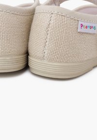 Zapatos slip-on de lona beige con un acabado texturizado, banda elástica y suela ligera de goma. Etiqueta de la marca cosida en un estilo colorido.