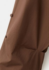 Tissu marron avec un seul bouton rond cousu près du bord, montrant la texture et de légers plis.