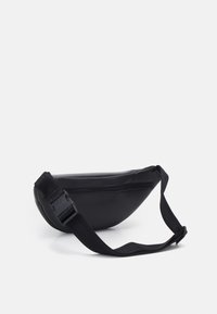 Czarna nylonowa saszetka na biodra o zakrzywionym kształcie, z regulowanym paskiem i zamknięciem na suwak. Charakteryzuje się minimalistycznym stylem i gładką fakturą.