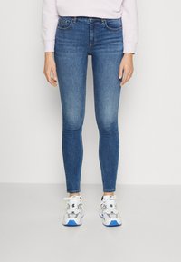 Jeans de mezclilla azul ajustados con una textura suave y un ligero desgaste. Combinados con zapatillas deportivas blancas y grises que tienen acentos azules.