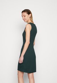 Vestido justo sem mangas em tecido verde profundo, apresentando uma cintura definida e uma bainha até aos joelhos, textura suave e design minimalista.