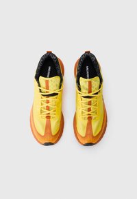 Des chaussures de sport à lacets avec un design jaune et orange, une tige en maille texturée et une semelle en caoutchouc avec des motifs de lignes diagonales.