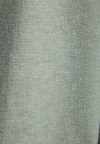 Vaaleanvihreä teksturoitu kangas, jossa on hillitty raitakuvio. Pinta näyttää pehmeältä ja hieman karhealta, ja siinä on tasainen väri.