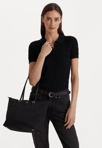 Svart kabelstickad polo med krage, kombinerad med högmidjade svarta jeans och en svart handväska med guldaccenter.