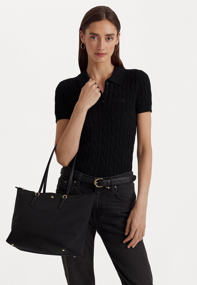 Svart kabelstickad polo med krage, kombinerad med högmidjade svarta jeans och en svart handväska med guldaccenter.