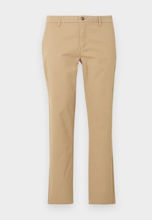 Beežid sirge lõikega püksid vööaasa, eesmine nööp ja tõmblukk, esitletud ühtlasel heledal taustal.