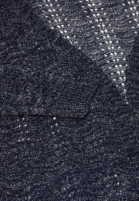Tessuto a maglia blu navale con un motivo a trama aperta, caratterizzato da una superficie testurizzata e irregolare e un leggero luccichio proveniente da filamenti metallici.