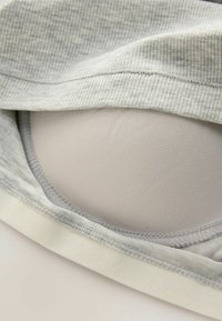 Grå, ribbad tyg delvis täcker en slät, beige bh-kopp, med ett mjukt, vitt elastiskt band i botten och fina sömnadsdetaljer.