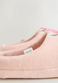 Weiche rosa Hausschuhe zum Hineinschlüpfen mit flauschiger Textur und einem "NEXT" Markenetikett an der Seite, in Seitenansicht gezeigt.