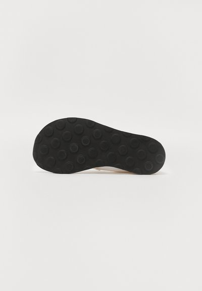 Sort gummisål med et mønster af cirkulære buler, flad design, glatte kanter og uden synlig branding eller accenter.