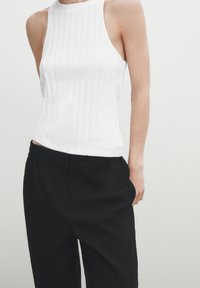 Canottiera bianca a costine con scollo alto abbinata a pantaloni neri larghi con vita elastica. Design semplice e strutturato.