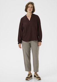 Top bordeaux a maniche lunghe con scollatura a volant, abbinato a pantaloni grigi chiari texture e sneakers marroni e crema.