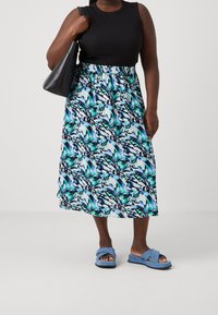 Mustat hihattomat yläosat on yhdistetty siniseen, valkoiseen ja vihreään kuvioituun midihameeseen, jota täydentävät siniset ristittävät sandaalit ja musta laukku.