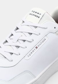 Baskets blanches avec dessus synthétique lisse, languette en mesh respirant, lacets plats et étiquette logo. Accents texturés et semelle cup.