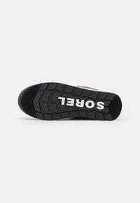 Sort gummisåle til sneakers med fremtrædende traktionsmønster, der har oprejst tekst "SOREL" i hvid. Tekstureret med riller og kanter.