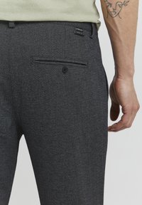 Pantalones gris ajustados de una tela texturizada, con un bolsillo trasero con botón y una pequeña etiqueta de marca cerca de la cintura.